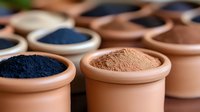 Natural clay bowls filled with vibrant mineral pigment powders in blue and brown tones, arranged in rows showing organic dye ingredients for artisanal crafts.