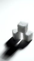 Stack of white sugar cubes on black spoon against white background, isolated for design use in food, nutrition, health and dietary content.