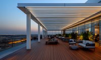 Luxurious rooftop terrace with wooden deck, modern pergola, and lounge furniture at sunset, featuring panoramic city views and ambient lighting.