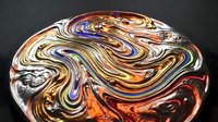 Colorful glass marble with swirling patterns in orange, blue, white and brown creating mesmerizing fluid art design on dark background.