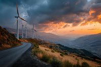 Wind turbines along mountain road at dramatic sunset with stormy clouds and golden light illuminating valley landscape. Renewable energy concept.