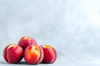 Fresh ripe nectarines with smooth red skin arranged on light gray background, selective focus. Natural organic summer fruits for healthy eating.