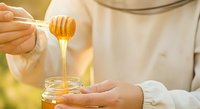 Closeup of hands drizzling golden honey from wooden dipper into glass jar, sweet organic food preparation and natural ingredient for cooking.