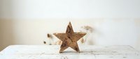 Rustic wooden star decoration on white distressed table with soft neutral background for seasonal home decor and craft projects.