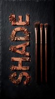 Crushed copper eyeshadow powder arranged in vertical strokes with three professional makeup brushes on dark slate background for cosmetics and beauty design projects.