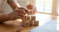Woman hands arranging wooden blocks with healthcare medical icons symbols on desk for wellness concept and insurance planning services.