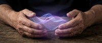 Senior man hands protecting glowing purple energy sphere on wooden table representing healing power, spiritual protection and mystical energy concepts.