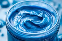 Swirling blue cosmetic cream texture in glass jar, macro shot showing luxurious moisturizer with smooth glossy surface and rich creamy consistency.