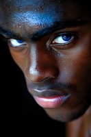 Close-up portrait of young African woman with artistic blue metallic makeup and water droplets on dark skin for beauty and fashion concepts.