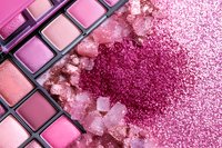 Crushed pink eyeshadow palette with scattered powder and crystals on pink background, close up macro shot showing texture and shimmer of cosmetic products.
