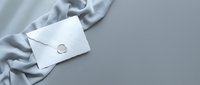 White envelope with wax seal on elegant gray silk fabric background for luxury correspondence and wedding invitations.