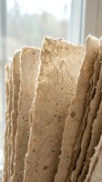 Handmade natural paper sheets with organic texture and fiber details arranged vertically near window for crafting and artistic projects.