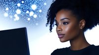 Young African American woman with natural curly hair working on laptop computer against blue bokeh lights background for technology and business concepts.