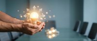 Businessman hands holding glowing light bulb with gear mechanism representing innovation and creative problem-solving in modern office environment.