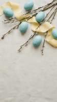 Speckled blue Easter eggs with pussy willow branches and yellow ribbon on neutral background for spring holiday decorations and greeting cards.