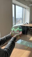 Person in gray sweater holding glowing holographic sphere displaying stress level balanced with waveform graphic in modern office with city skyline view through windows, representing wellness technology and mental health monitoring.