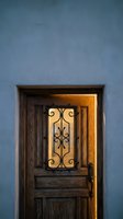 Rustic wooden door with ornate iron scrollwork glowing warmly against blue stucco wall creating inviting entrance with traditional southwestern charm.