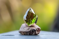 Green crystal mineral specimen on rough stone base against soft blurred natural background, showcasing gemstone clarity and facets in natural lighting.