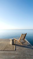 Wooden deck chair on pier overlooking calm blue sea and clear sky, ideal for travel, vacation, relaxation and resort marketing materials.