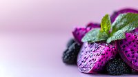 Fresh purple dragon fruit slices with mint leaves and blackberries on soft pink background, selective focus creates dreamy mood for food photography and design.