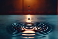 Water droplet creating ripples on calm surface with warm orange and blue lighting effects for meditation and tranquility concepts.