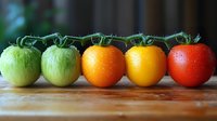 Fresh tomatoes in different ripening stages from green to red arranged in row on wooden surface, showing natural color progression with water droplets.