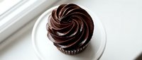 Decadent chocolate cupcake with rich swirl frosting on white plate, perfect for bakery menus, dessert blogs, and sweet treat marketing materials.