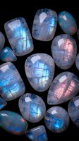 Polished moonstone gemstones with iridescent blue and pink flashes scattered on black background for jewelry design and crystal healing practices.
