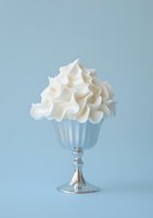 Whipped cream dessert served in elegant glass goblet against soft blue background, perfect for food and beverage advertising.