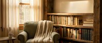 Cozy reading corner with comfortable armchair, soft throw blanket and built-in bookshelf filled with books in warm home library interior for relaxation.