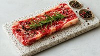 Raw beef steak with rosemary and peppercorns on stone cutting board, ready for cooking gourmet meal.