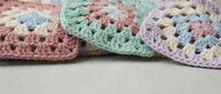 Colorful crocheted granny squares in pastel pink, green and purple yarn with intricate stitching patterns for handmade crafts and textile projects.