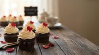 Chocolate cupcakes with vanilla frosting and red heart decorations on rustic wooden table for Valentine's Day celebration and romantic dessert occasions.