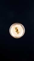 Gold flakes suspended in clear resin within a glass container, isolated against dark background for design, jewelry, and craft projects.