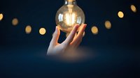 Hand holding glowing light bulb with warm bokeh lights in dark background symbolizing innovation creativity and bright ideas for business concepts.
