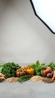 Fresh organic vegetables and herbs arranged on concrete surface with natural lighting for healthy cooking and nutrition concepts.