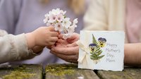 Child giving white flowers to mother with Happy Mother's Day card, celebrating family love and appreciation on special holiday occasion.
