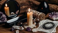 Mystical fortune telling setup with burning candles, tarot cards, crystals, mirror and gemstones on wooden surface for spiritual divination practices.