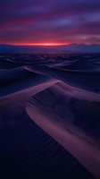 Dramatic desert dunes bathed in vibrant purple and pink sunset light, with rippled sand patterns creating depth across the landscape. Perfect for travel, nature, and atmospheric backgrounds.