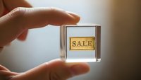 Hand holding transparent glass cube with golden sale label inside for retail marketing and promotional campaigns.