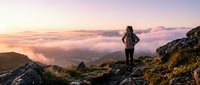 Hiker with backpack standing on mountain peak at sunrise overlooking misty valley landscape, adventure travel and outdoor exploration concept for hiking and trekking.
