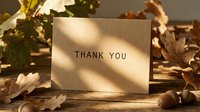Kraft paper thank you card surrounded by autumn oak leaves and acorns on rustic wood, warm sunlight shadows, fall seasonal greeting concept.