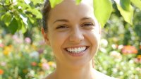 Happy young woman smiling outdoors in natural sunlight with green foliage background for wellness and lifestyle content.