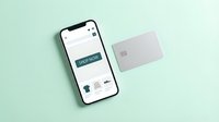 Smartphone displaying online shopping app with shop now button beside a credit card on mint green background for e-commerce concepts.