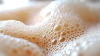 White soap foam bubbles in macro photography showing delicate texture and patterns with soft beige tones, creating abstract background for spa and wellness designs.