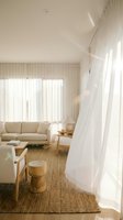 Bright minimalist living room with cream sofa, wooden furniture, natural fiber rug, and flowing white sheer curtains filtering sunlight through glass doors for modern home decor.
