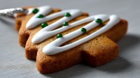 Christmas tree shaped gingerbread cookie with white icing drizzle and green sprinkles on wooden surface, perfect for holiday baking and festive treats.