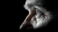 Dramatic close-up side view of human eye in black and white with selective lighting highlighting eyelashes, skin texture and iris detail against dark background.