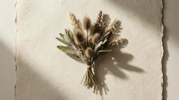 Dried wildflower bouquet with wheat, teasel, and eucalyptus on textured paper background, casting soft natural shadows in warm neutral tones.