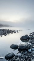 Misty coastal landscape with smooth water and scattered boulders along rocky shoreline, ideal for nature and seascape projects.